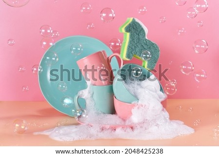 creative still life in bright colors with a sponge in the shape of a unicorn. The unicorn will say through the mountains of dirty dishes filled with foam for washing dishes surrounded by soap bubbles Royalty-Free Stock Photo #2048425238
