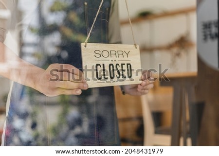 Close-up shot of a closed sign in front of a storefront, a café employee standing holding a store opening-closing sign, flipping over a sign that says "closed". Cafe food and beverage service concept.