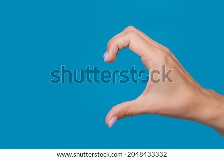 Close-up color photography of female caucasian hand isolated on blue background. Young adult woman forming shape of half of heart with her fingers. Point of view shot with copy space Royalty-Free Stock Photo #2048433332