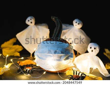 A pumpkin in a protective mask and white ghosts in the background. Halloween celebration concept. Selective focus. Close-up.