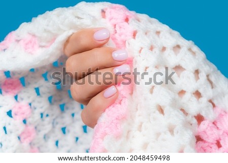 Close-up top view color stock photography of elegant minimal pastel pink natural manicure. Female hands isolated on warm soft fluffy cozy blanket background. Nail design with cute white hearts