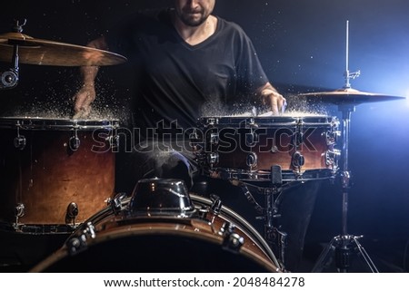 A male drummer plays drum sticks on a snare drum with splashing water in a dark room. Royalty-Free Stock Photo #2048484278