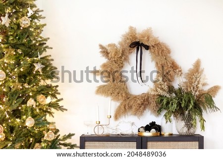 Assorted stylish decorations placed on shelf and wall near Christmas tree with bright fairy lights and stylish baubles at home