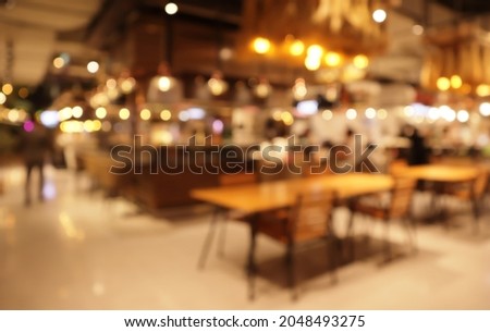 Abstract blurred food court interior. Bokeh with golden yellow lighting, color brown wooden table. Warm tones in blur background. Restaurant tables empty in a shopping mall Royalty-Free Stock Photo #2048493275
