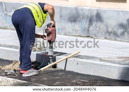 A worker makes a hole in the asphalt with a perforator in order to install a road sign. Road works.