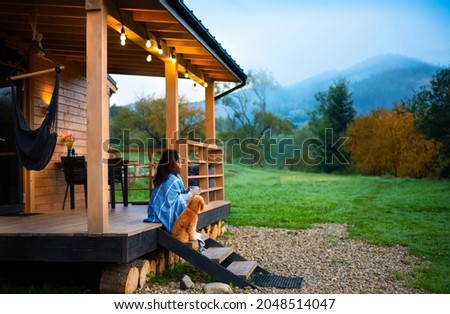  Woman with dog resting on the terrace mountain chalet at sunset. Royalty-Free Stock Photo #2048514047