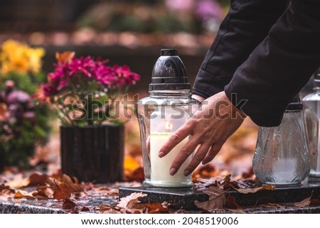 Woman is putting candle lantern at grave in cemetery. Grief and paying respect for dead person Royalty-Free Stock Photo #2048519006