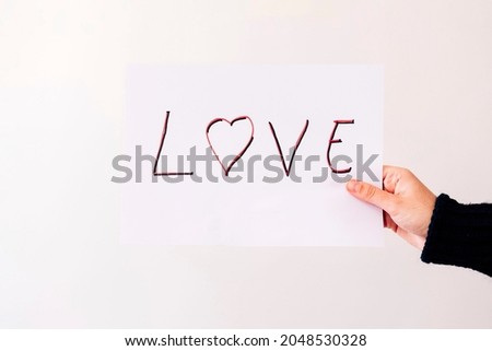Hand holds a poster with the word LOVE on white background. Love concept.