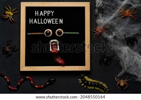 spider web, snakes, insects made of candy and marmalade on a black background, Halloween, top view. happy halloween text.