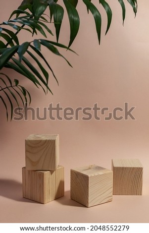 wooden cubes still life against pale pink background with blurred palm leaves
