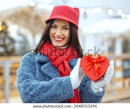 Emotional brunette woman in winter coat holding a gift box at christmas fair