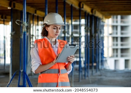 Female construction engineer. Architect with a tablet computer at a construction site. Young Woman looking, building site place on background. Construction concept. Royalty-Free Stock Photo #2048554073