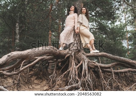 The unity of man and nature. Creative photo of two sisters among the roots of trees. A place for text. Women in light skirts and sweaters