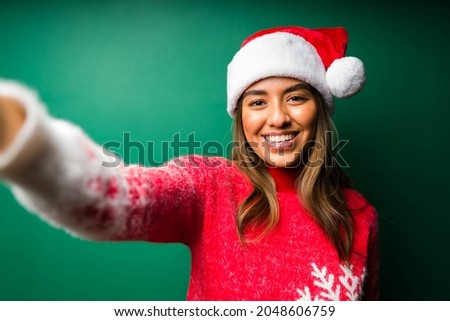 Personal perspective of a gorgeous woman taking a selfie with a santa hat against a green background