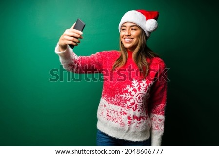Posting on social media. Attractive latin woman taking a selfie with a smartphone while celebrating Christmas 