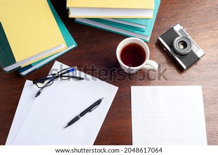 books on a desk with a cup of tea, blank sheets, glasses and a pen and a camera