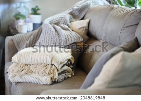 Stack of a variety of soft knit throw blankets stacked on a grey couch in a farmhouse style living room. Selective focus on covers with blurred foreground and background. Royalty-Free Stock Photo #2048619848