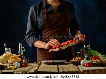 Ingredients for Caesar salad. Cooking. The chef is cutting tomatoes on a cutting board. Wooden texture. Dark blue background. Restaurant, hotel, cookbook, step by step recipe.