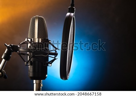 Professional black microphone and pop filter on a beautiful multicolored background. Clean sound, vocals, conversational genre, instrumental music. Sound recording studio.