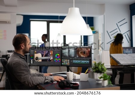 Video editor cuting footage working at film editing montage on computer with dual monitors setup in multimedia creative agency office. Videographer man processing film using post production software