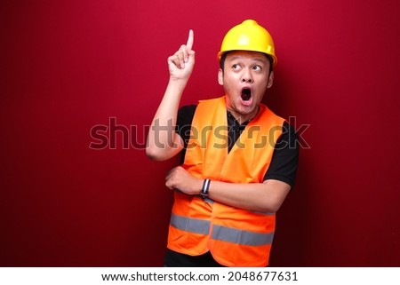 Shock Young asian man worker is surprised and shouting wow with pointing above with his hand isolated on red background.