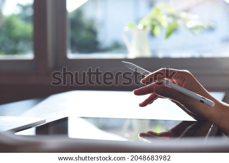 Female graphic designer with stylus pen using digital tablet and finger touching on tablet screen on table, close up. Business woman working on digital tablet at home office, work from home concept