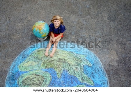 Little preschool girl with earth globe painting with colorful chalks on ground. Positive toddler child. Happy earth day concept. Creation of children for saving world, environment and ecology.