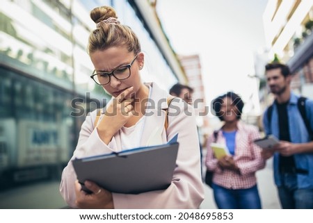 Young woman holding books while standing on background of university and friends.