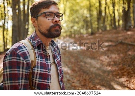 Caucasian hipster male model outdoors in nature. Colorful landscape with trees, rural road, orange and red leaves, sun in autumn.