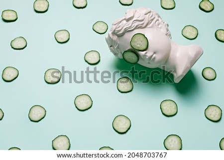 Fresh cucumber slices pattern and ancient bust with a cucumber slice mask on eyes on green background. Creative beauty concept. Spa beauty treatments at home, body care concept, organic cosmetics. Royalty-Free Stock Photo #2048703767