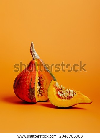 Nutmeg fresh pumpkin with cut slice isolated on the vibrant orange background. Creative fall food concept. Minimal Halloween or Thanksgiving decoration. Autumn backdrop with copy space.