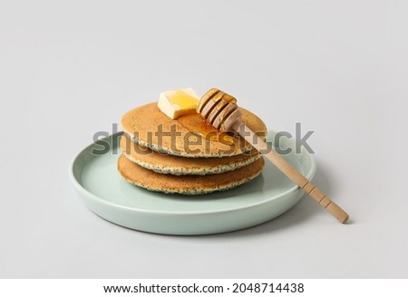 Plate of tasty pancakes with honey and butter on light background