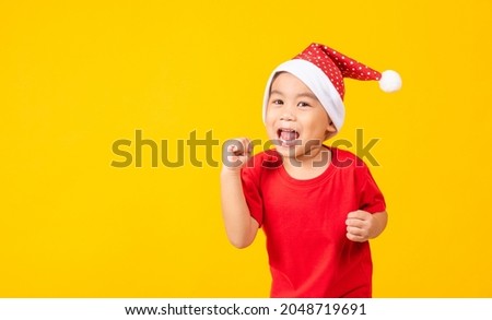 Kid dressed in red Santa Claus hat, Portrait of Asian little cute boy smile and excited the concept of holiday Christmas Xmas day or Happy new year, studio shot isolated on yellow background