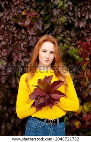 Autumn. Portrait of a beautiful happy red-haired girl in a yellow jumper among the autumn leaves. Color. Atmosphere. A place for text. High quality photo