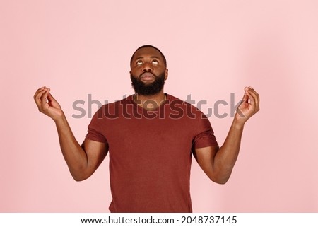 Tranquil African-American guy actor with beard in brown t-shirt meditates  looking upward standing on pink background in studio close view