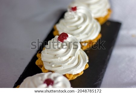 many festive cakes with whipped cream stand in a row on the table on a green background close up