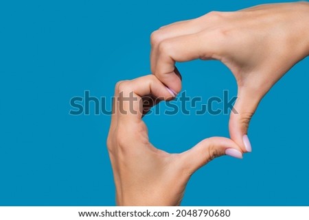 Horizontal color photography of white young adult woman making heart gesture with 2 hands isolated on bright blue background