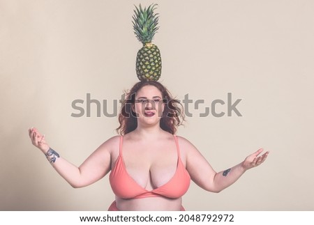 Woman versus pineapple. Curvy girl having fun with ananas over her head