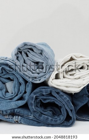 Stack of rolled blue and white jeans on a white background. Vertical shot. Free space above the pile. Jeans industry. Sale concept.