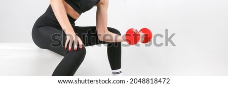 female athlete poses with a dumbbell on a light gray background, studio shot. a sporty woman wearing black sportswear holds a red dumbbell. conceptual photo of women sport exercises. 