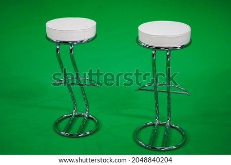Empty bar stools stand in a greenscreen studio.