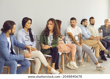 Groups of serious people of different ages talking and having discussions while sitting in queue by office wall waiting for job interview, public lecture, training session, audition or business event Royalty-Free Stock Photo #2048840678