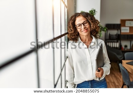 Middle age hispanic woman smiling confident holding clipboard at office Royalty-Free Stock Photo #2048855075
