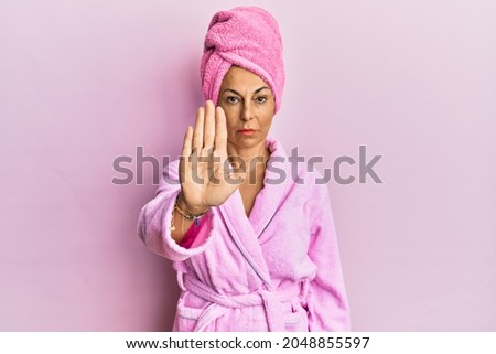 Middle age hispanic woman wearing shower towel cap and bathrobe doing stop sing with palm of the hand. warning expression with negative and serious gesture on the face. 
