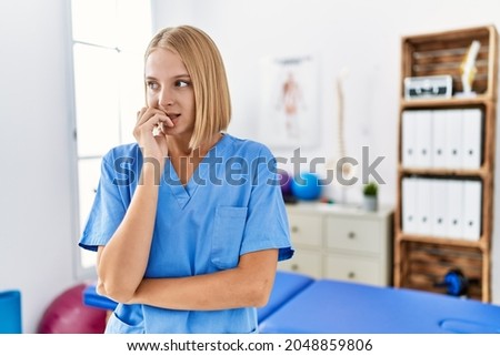 Young caucasian physiotherapist woman working at pain recovery clinic looking stressed and nervous with hands on mouth biting nails. anxiety problem. 