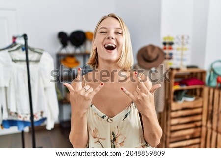 Young caucasian woman at retail shop shouting with crazy expression doing rock symbol with hands up. music star. heavy concept. 