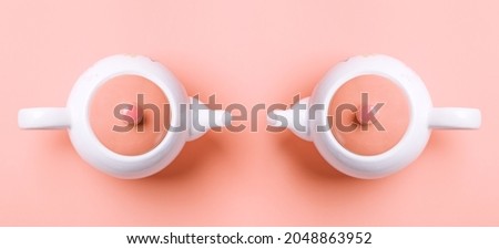 Banner. Two white porcelain teapots with a pink lid on a pink background. Flat lay. Copy space. Concept of female health and Breast Cancer Awareness Month. Royalty-Free Stock Photo #2048863952