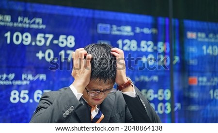 Depressed businessman in front of an electric bulletin board. Japanese translation:"usa dollar yen","canada dollar yen","euro yen","pound","rmb yen"