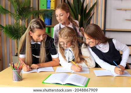 A young schoolgirl in a school uniform writes in a notebook. The child prepares lessons at the table. Girl writes in a notebook. Children in the classroom. School collective