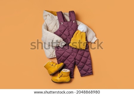 Puffer jacket, warm  pants hat and boots on orange background. Set of baby clothes for  winter. Fashion kids outfit.
